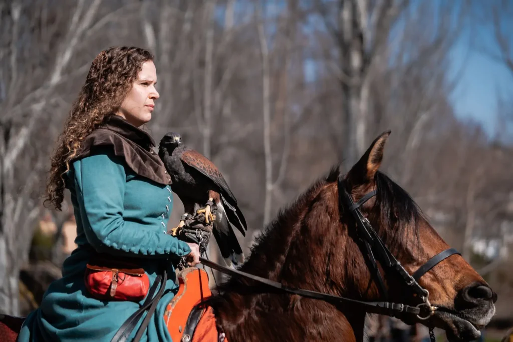 Cetrera medieval montada a caballo con ave rapaz durante recreación histórica